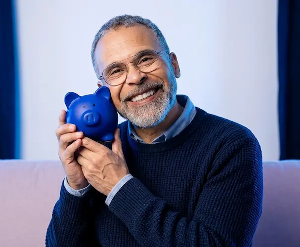 Hombre adulto sonriendo mientras sostiene una alcancía, como referencia a los usos de un CDT además del ahorro